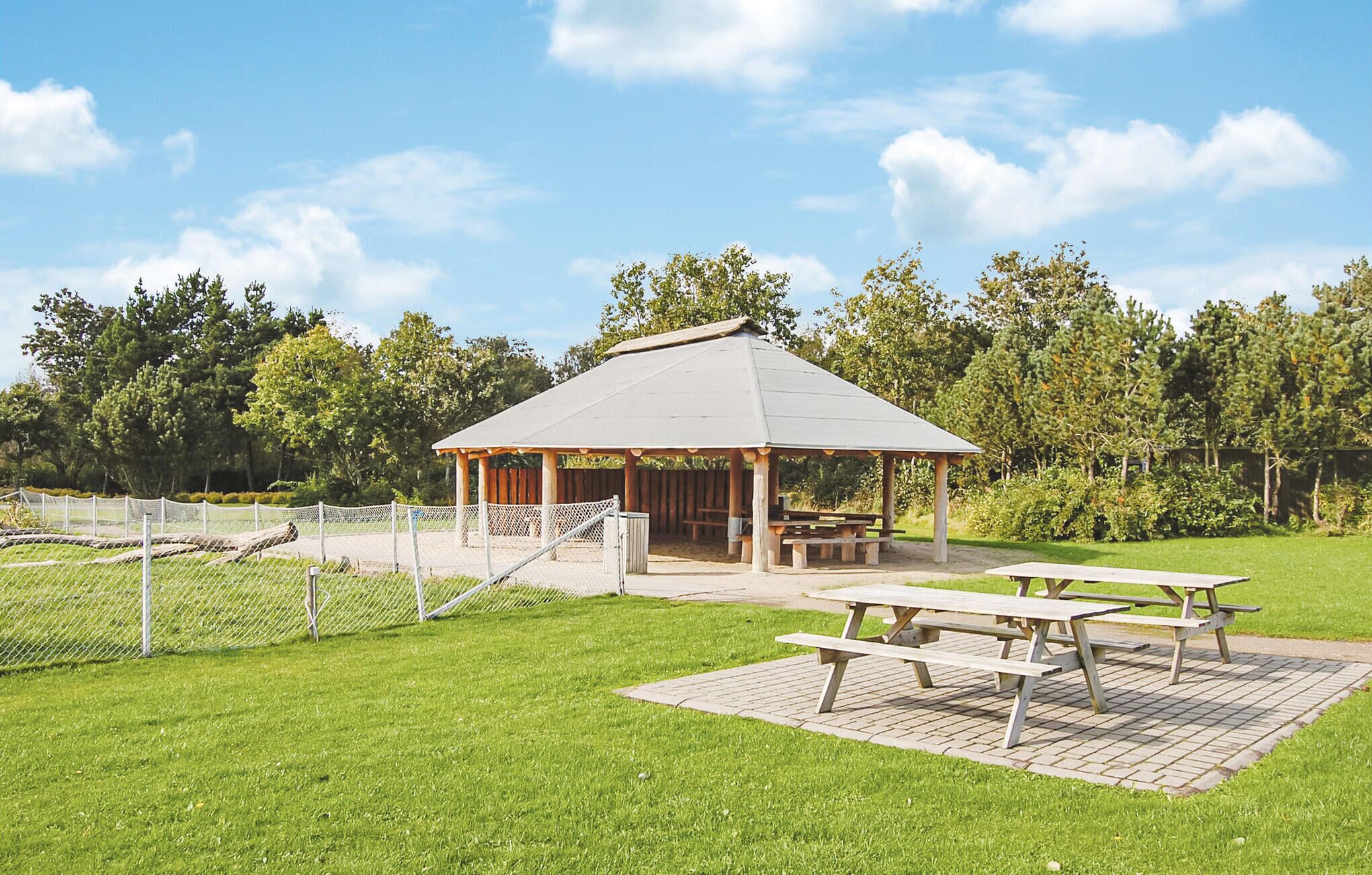 Un pavillon doté d’un toit, entouré d’une zone délimitée par une clôture et comprenant des tables de pique-nique.