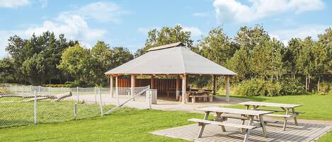 Un pavillon doté d’un toit, entouré d’une zone délimitée par une clôture et comprenant des tables de pique-nique.