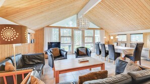 Un vaste espace de vie doté d’un haut plafond, de murs en bois, d’une grande fenêtre et d’une table à manger avec des chaises.
