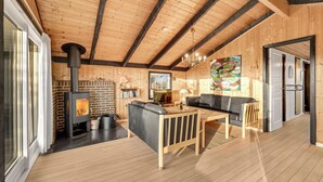 Un accogliente interno di una baita con camino, pareti in legno, un divano e zona pranzo.