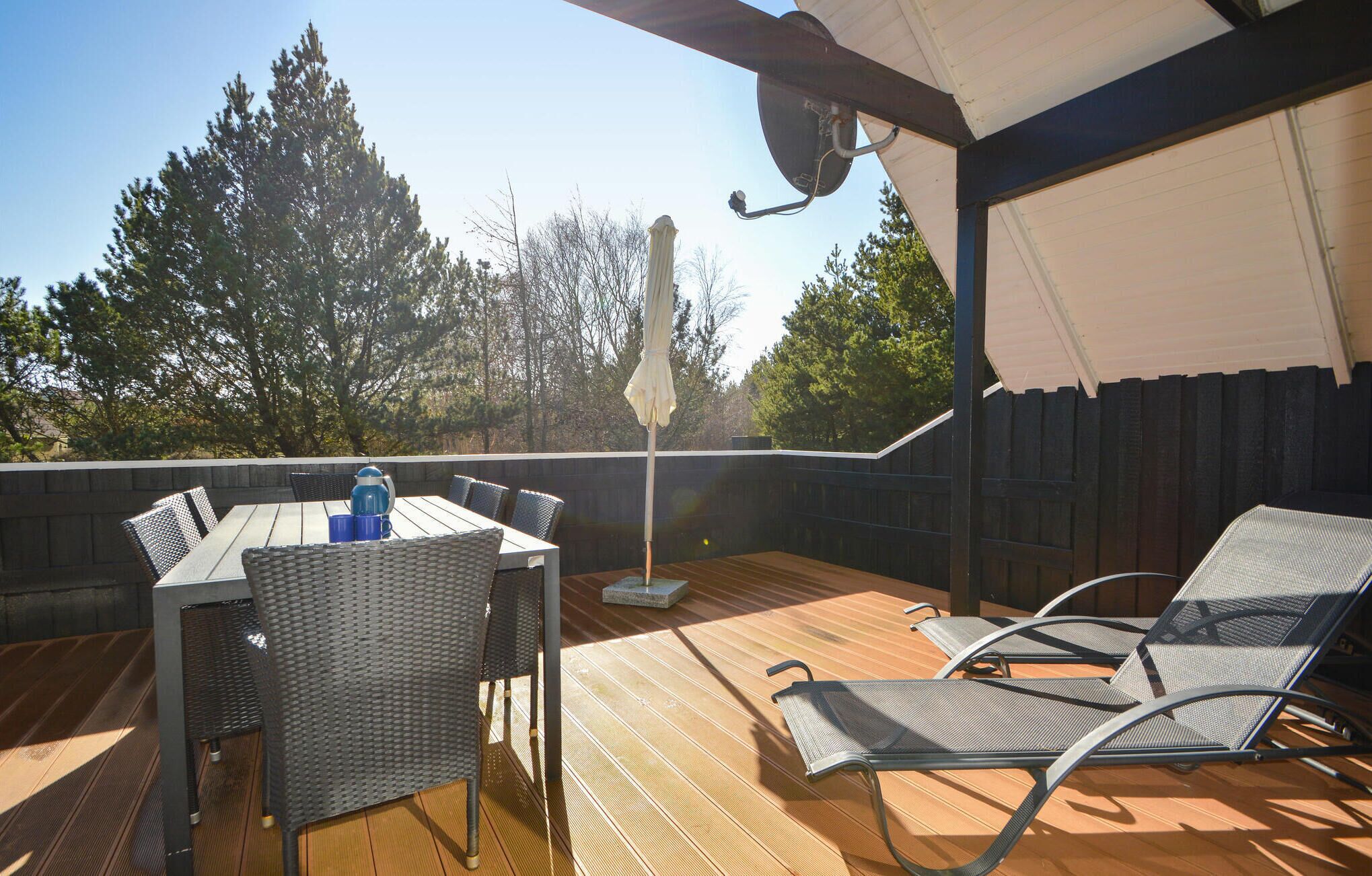 A wooden deck with a table and chairs, an umbrella, and a view of trees.