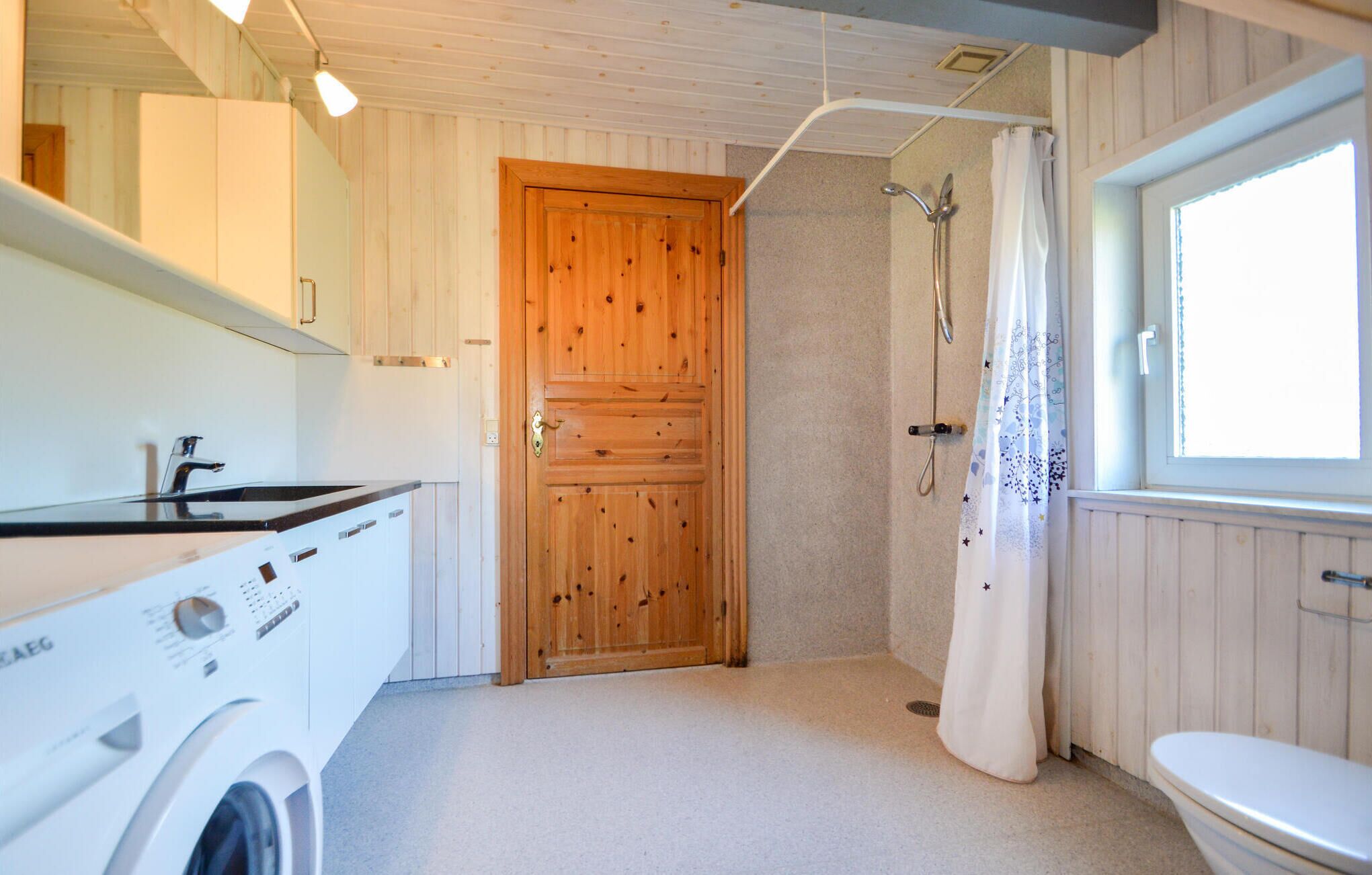 Een kleine badkamer met een houten deur, een douche, toilet en een wasmachine.