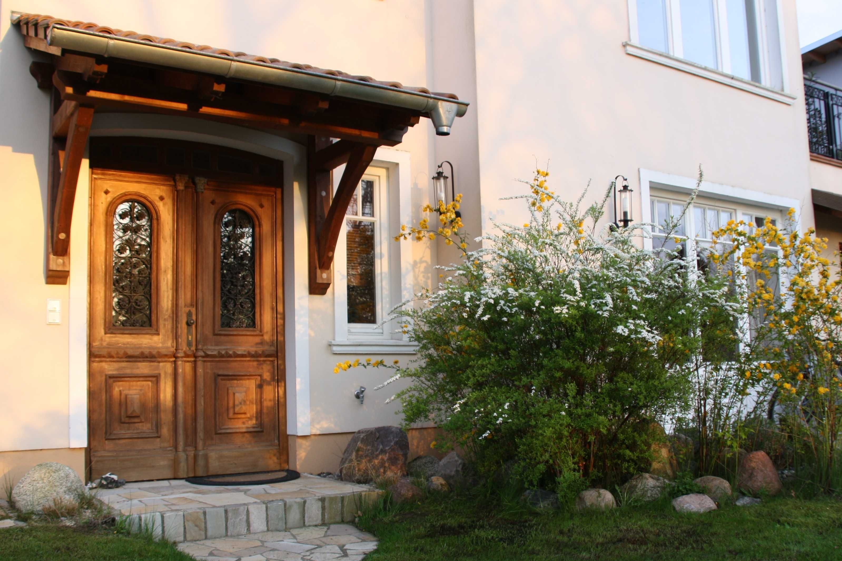 A house with a wooden front door, a stone pathway, and a garden with rocks and yellow flowers.
