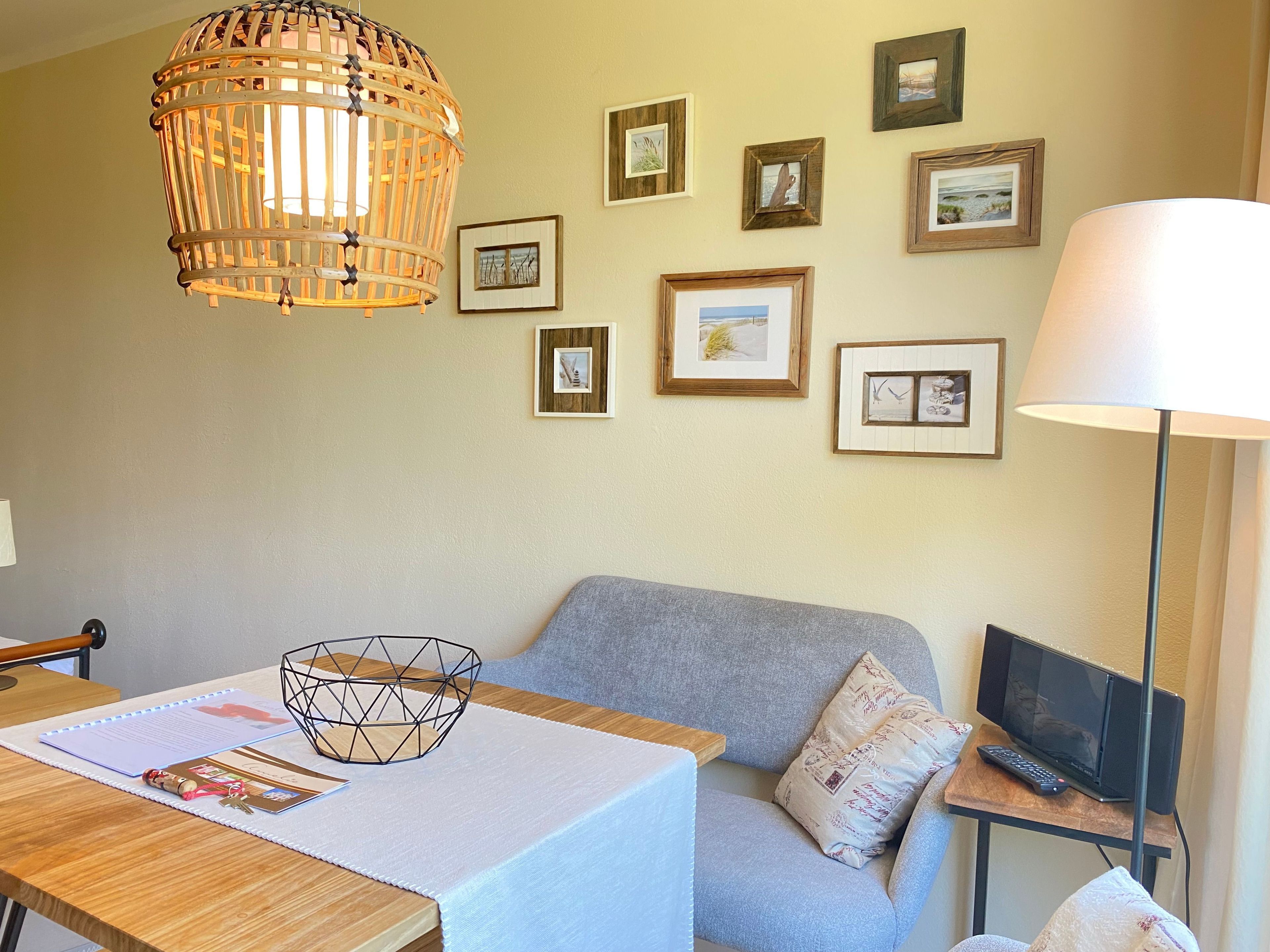 Une pièce avec une table en bois, un canapé gris, un ordinateur portable posé sur une petite table d’appoint et un luminaire suspendu.