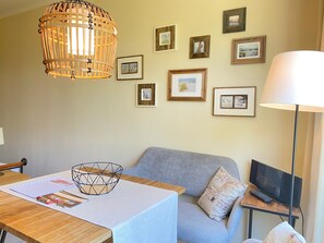 Une pièce avec une table en bois, un canapé gris, un ordinateur portable posé sur une petite table d’appoint et un luminaire suspendu.