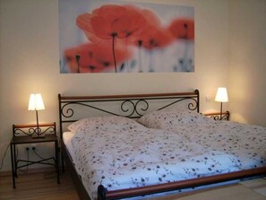 Une chambre à coucher avec un lit, deux lampes de chevet et un tableau représentant des fleurs accroché au mur.