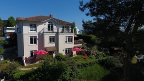 Ein zweistöckiges Haus mit Balkon und einem Garten inklusive Terrasse, sowie einem roten Sonnenschirm.