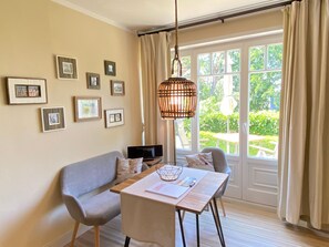Une pièce avec un canapé, une table sur laquelle se trouve un ordinateur portable, des tableaux encadrés au mur et une vue sur la verdure à l’extérieur.