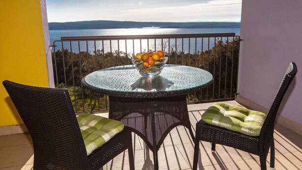 Ein runder Glastisch mit Obstschale auf einem Balkon mit Seeblick und Bergblick.