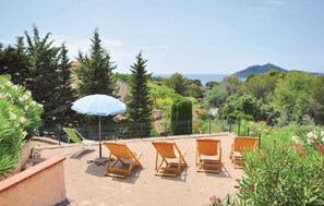 A patio with four wooden lounge chairs and a blue umbrella, surrounded by greenery and overlooking a scenic landscape. - Domaine de la Bastide d'Agay (Agay)
