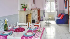 Un coin repas avec une table dressée pour quatre personnes, une cheminée, un canapé et une fenêtre avec des rideaux.