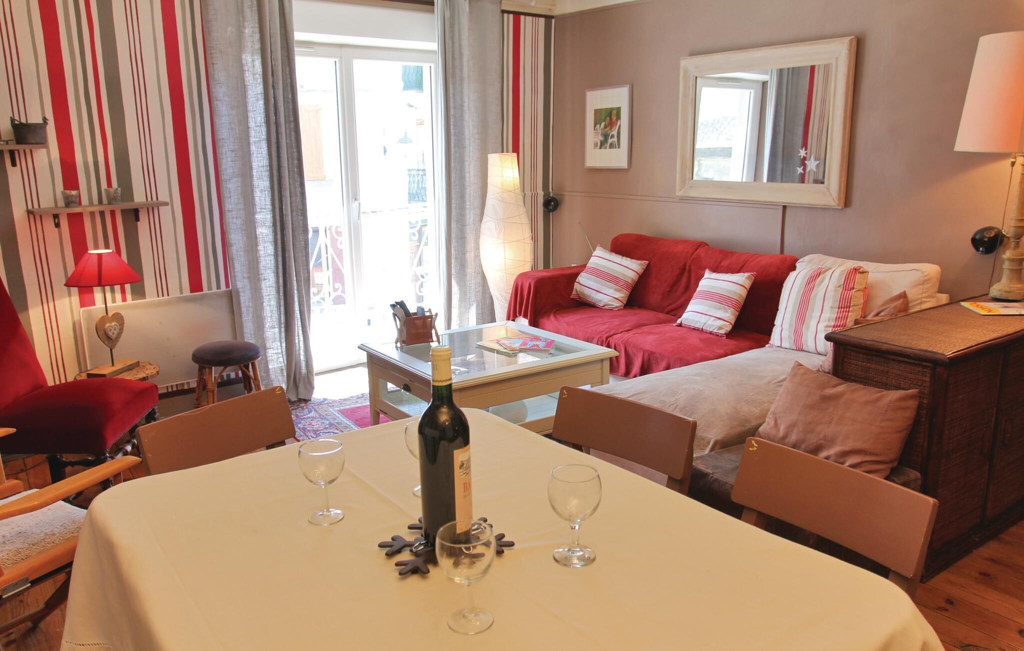 A cozy living room with a red sofa, a coffee table, and a dining table set with wine glasses.