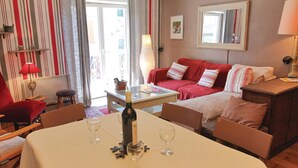 A cozy living room with a red sofa, a coffee table, and a dining table set with wine glasses.
