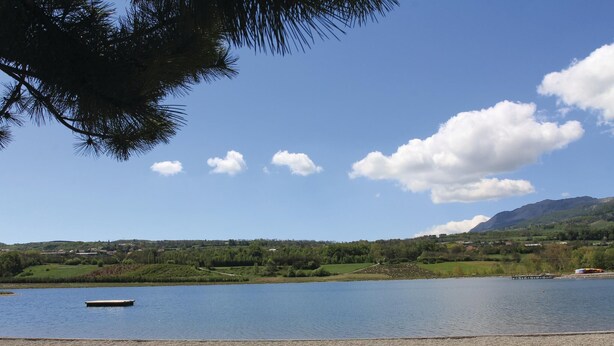A calm lake with a small dock, surrounded by green hills and a clear sky.