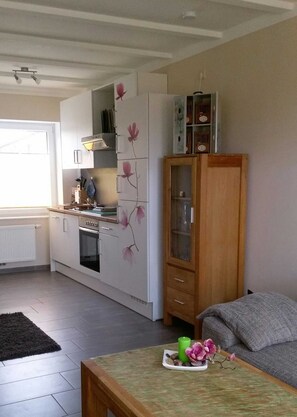 Eine moderne Küche mit weißen Schränken, einem Holzkabinett mit Glastüren und einem Essbereich mit Tisch und Sofa.