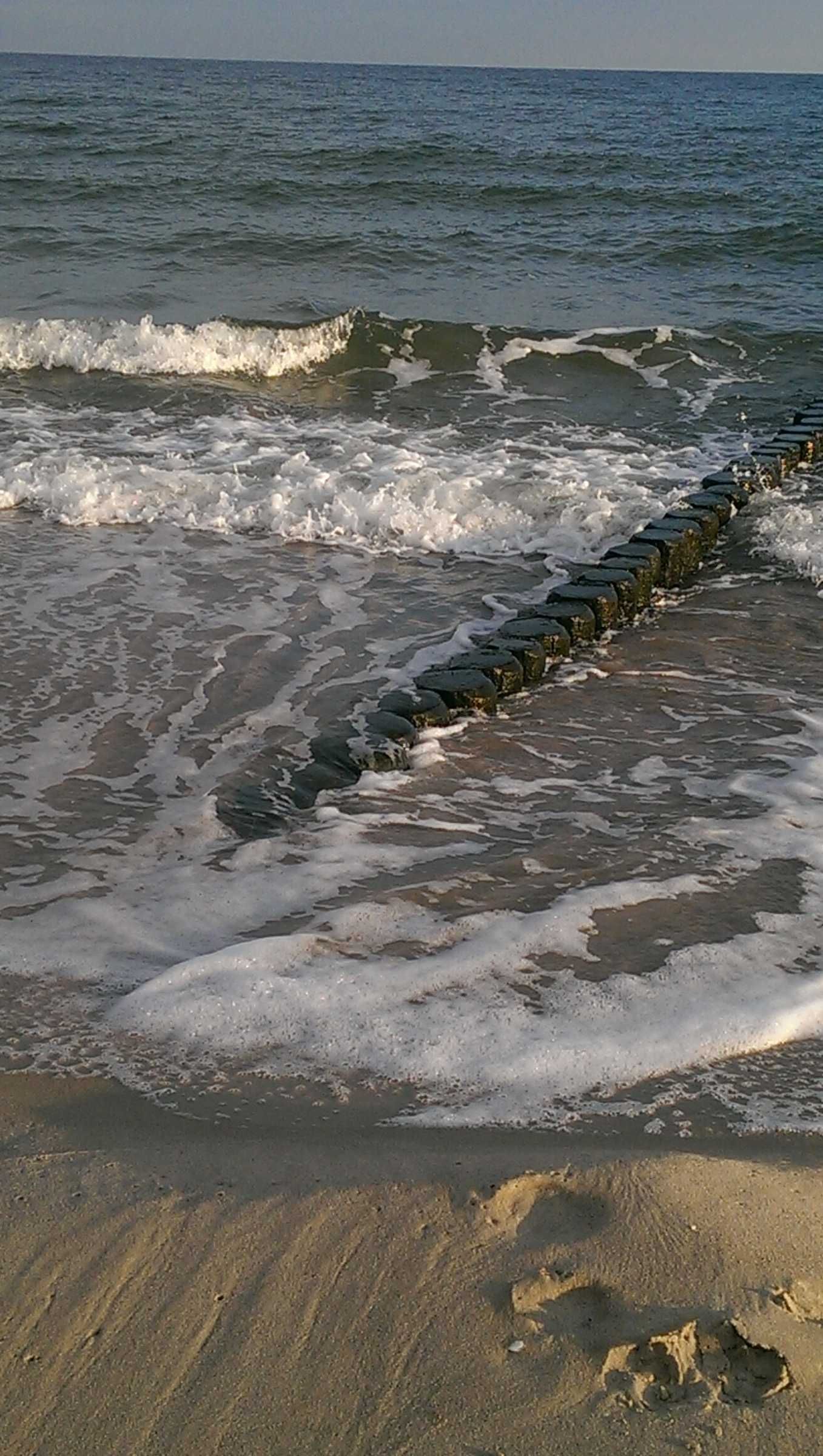 Een strand met golven, een stenen golfbreker en voetafdrukken in het zand.