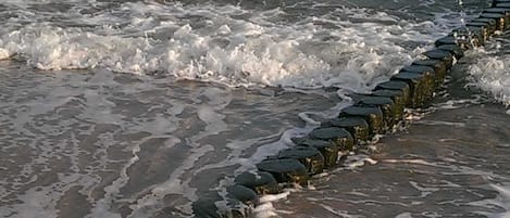 Een strand met golven, een stenen golfbreker en voetafdrukken in het zand.