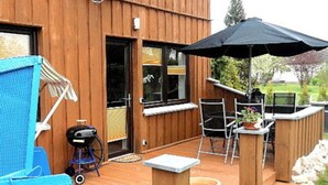 Eine Holzterrasse mit Grill, Sitzgelegenheiten und einem großen Sonnenschirm.