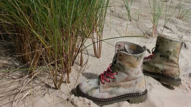 Ein Strand mit Sand, Gras und einem Paar Stiefeln.