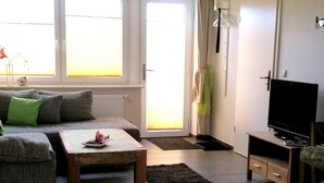 Ein Wohnzimmer mit Sofa, Couchtisch, Fernseher und einem großen Fenster.