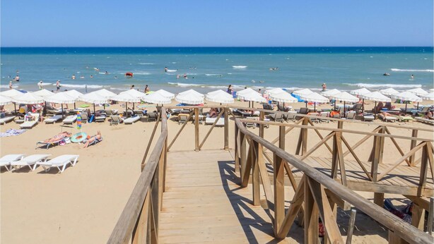 Un muelle de madera que conduce a una playa con sombrillas blancas y tumbonas.