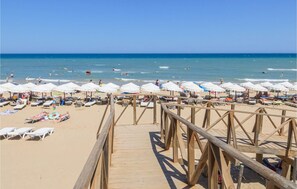 Une promenade en bois menant à une plage parsemée de parasols blancs et de chaises longues.