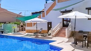 Una piscina con sillones de descanso y sombrillas, una escalera y un patio con mobiliario exterior.
