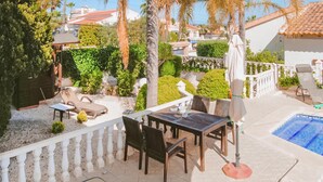 Un patio con mesa y sillas, piscina y barandilla blanca.