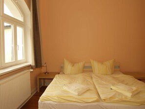 A bedroom with a large bed, two bedside tables, a window with curtains, and a radiator.