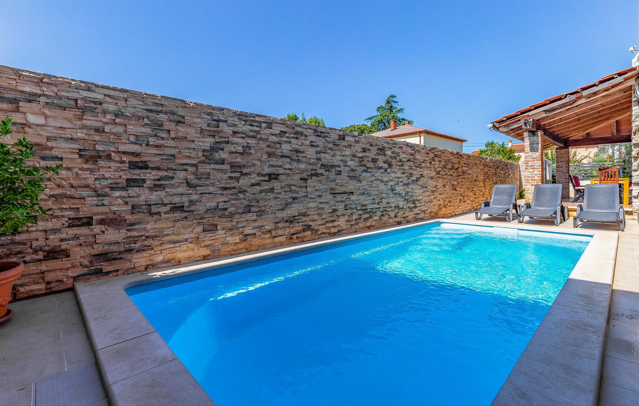 A swimming pool with stone walls and lounge chairs.