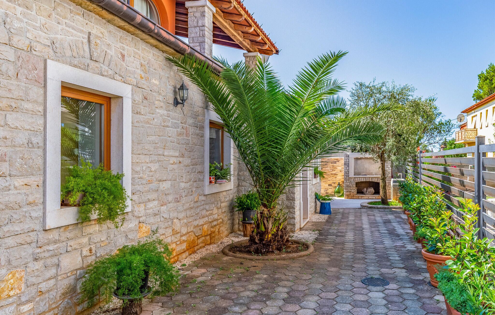 A narrow stone-paved courtyard with a stone wall, a wooden door, and a small garden area with potted plants.