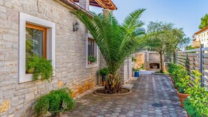 Un patio estrecho empedrado con pared de piedra, una puerta de madera y una pequeña zona ajardinada con plantas en macetas.