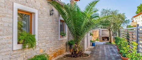 A narrow stone-paved courtyard with a stone wall, a wooden door, and a small garden area with potted plants.
