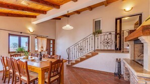 Un comedor con una mesa y sillas de madera, una escalera con barandales decorativos y una chimenea.