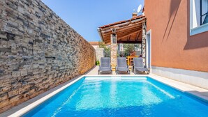 Una piscina con sillones de descanso, un muro de piedra y un edificio de fachada roja.
