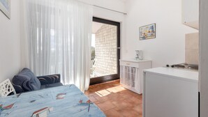 Cocina compacta con refrigerador, cafetera y lavamanos. Hay un comedor con mesa y sillas, y una ventana con cortinas translúcidas.
