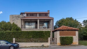 Una casa de dos pisos con un balcón, una estructura pequeña adosada con techo de tejas y un muro de piedra.