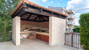 Una cocina al aire libre con techo de baldosas y paredes de piedra, rodeada por una cerca de metal y follaje.