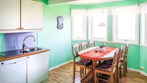 A dining area with a round table and chairs, a kitchen with a sink and cabinets, and a window with curtains. - Lovely home in Sveio with WiFi (Sveio)