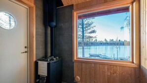 A room with a wood-burning stove, a window with a view of a lake, and a door with a round window.