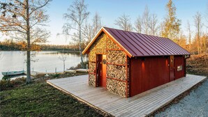 A small wooden cabin with a metal roof, situated on a wooden dock by a lake.