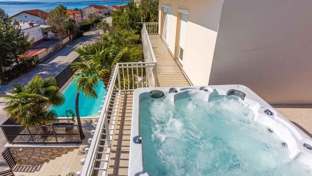Un balcon doté d’un jacuzzi et d’une piscine, entouré de palmiers et offrant une vue sur la mer.