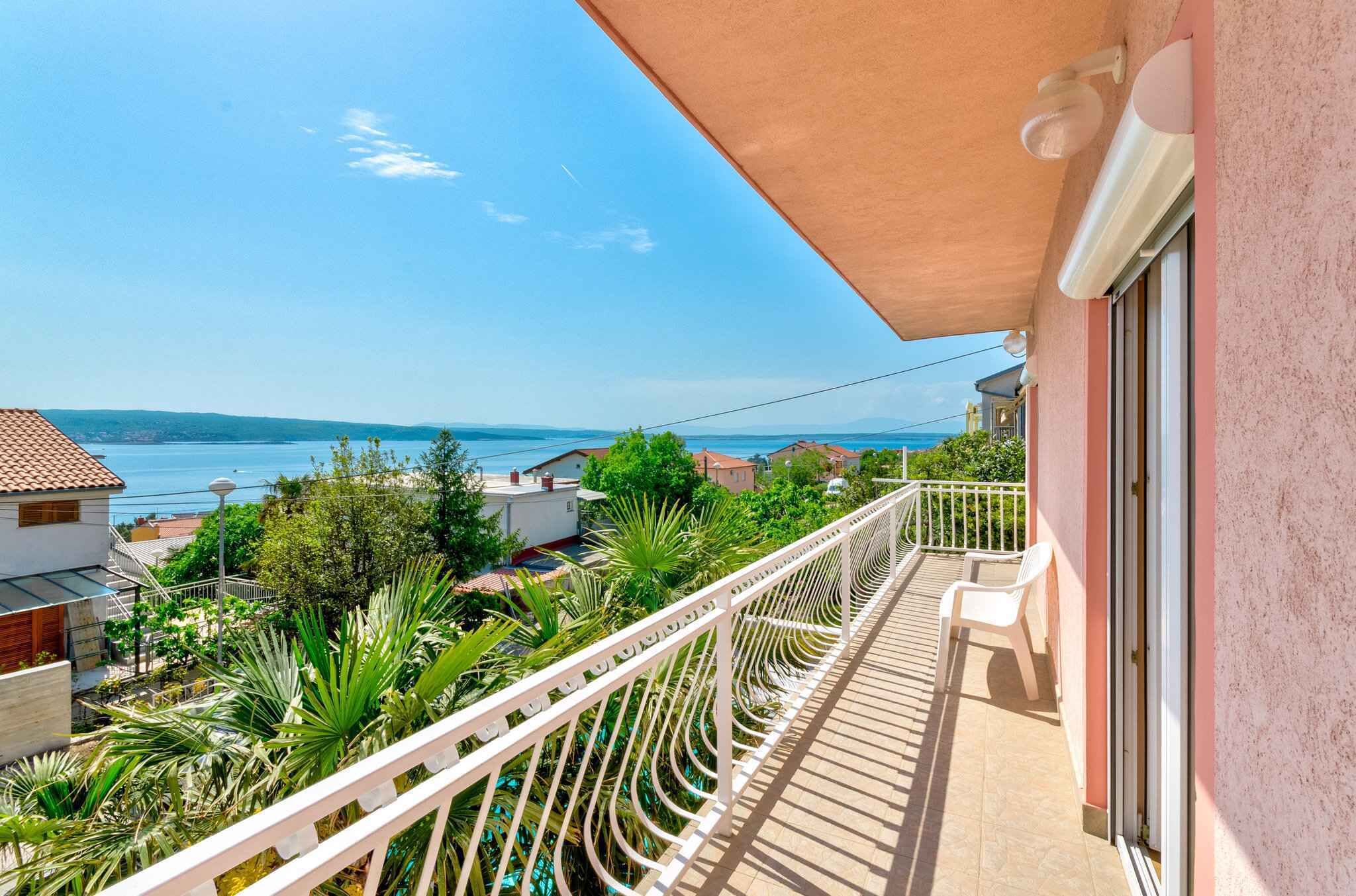 Varanda com vista para o mar e colinas, um corrimão branco e uma porta à direita.