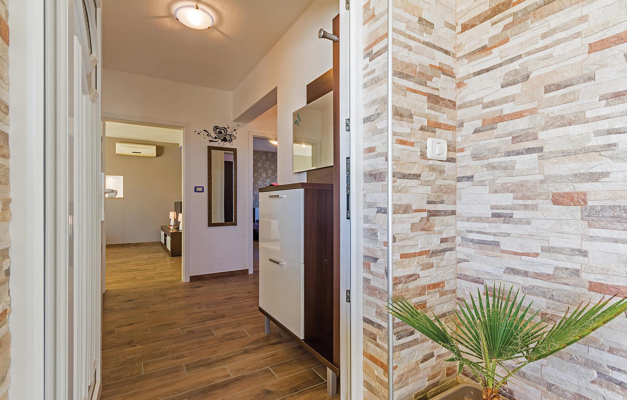 A hallway with wooden flooring, a white refrigerator, and a wall with a stone pattern.