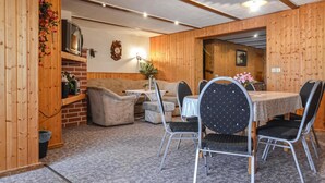 Una habitació acollidora amb interior de fusta, un sofà, una taula de dinar amb cadires i una petita cuina.