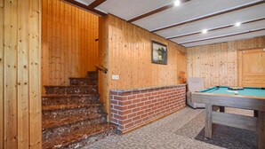 Un interior de fusta amb una escala, billar i una llar de pedra.