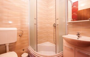 Een badkamer met een douchecabine van glas, een wit toilet en een wastafel met een spiegel erboven.