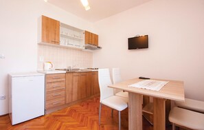 Een compacte keuken met houten kastjes, een witte koelkast, een spoelbak en een eettafel met twee stoelen.