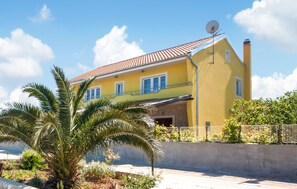 A yellow house with a red-tiled roof, a satellite dish, and a concrete wall in the foreground. - Stunning apartment in Sibenik with house sea view (Sibenik)