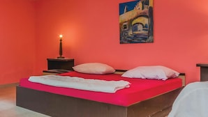 A bedroom with a red wall, a bed with a white blanket, two pillows, a nightstand with a candle, and a painting of a building. - Amazing apartment in Vrsar with WiFi (Vrsar)
